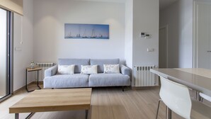 A modern living room with a grey sofa, a wooden coffee table, and a painting of sailboats on the wall. - ApartUP Patacona Beach Select (Alboraya)
