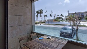 A room with a large window overlooking a parking area and a building. There is a wooden table with a chair, a small table with a cup and a notebook. - ApartUP Patacona Beach Select (Alboraya)