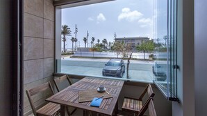 Un balcón con mesa y sillas, vista a un estacionamiento y un edificio al fondo.