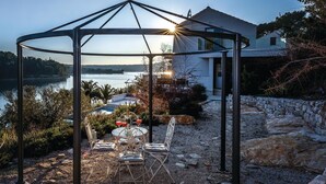 Ein Pavillon mit Tisch und Stühlen mit Blick auf einen See und ein Haus.