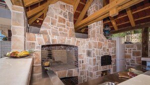 Ein Kamin aus Stein mit Backofen, Holzbalken und einer Obstschale auf der Arbeitsplatte.