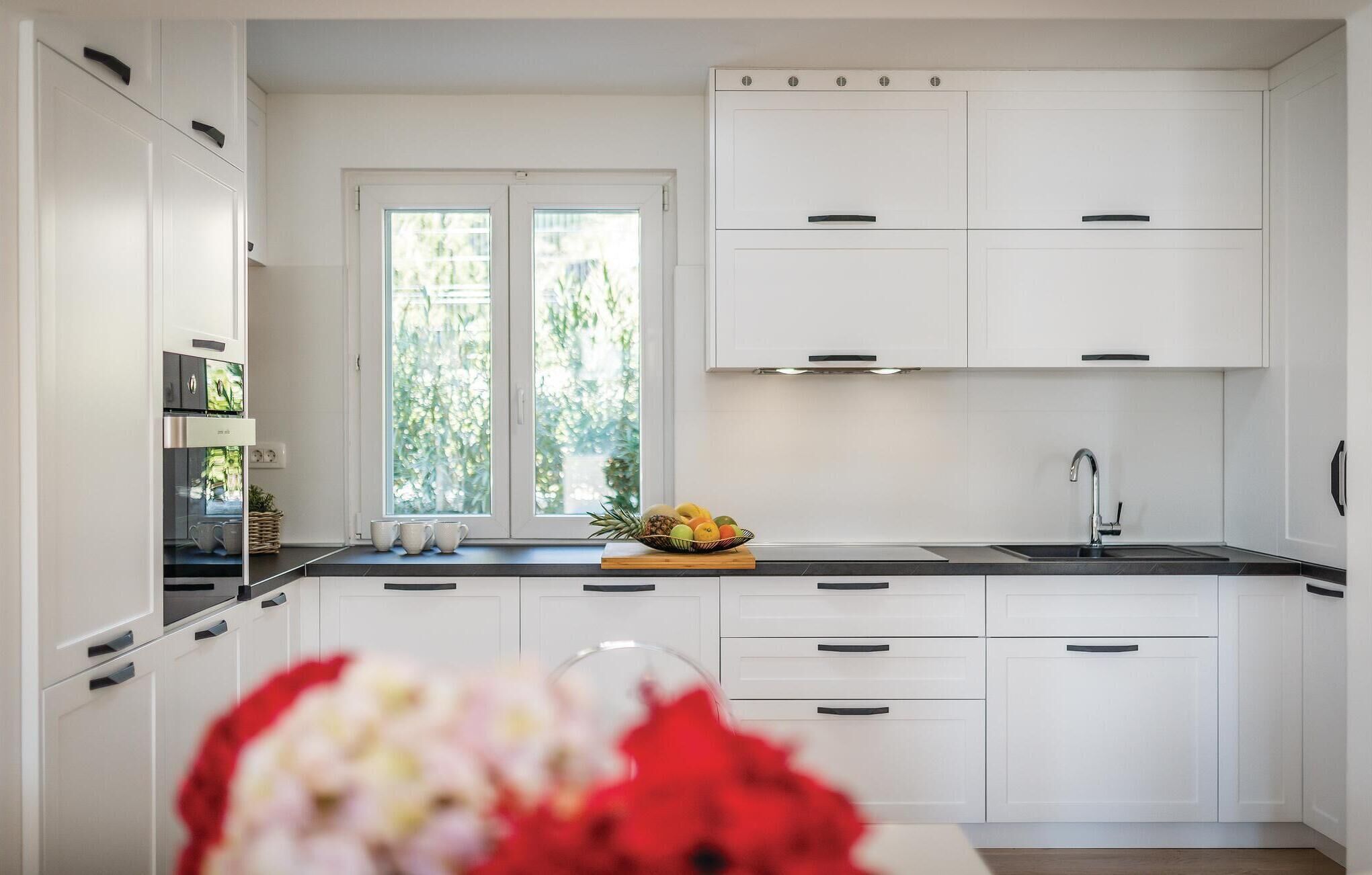 A modern kitchen with white cabinetry, a double sink, and a window with a view of greenery.