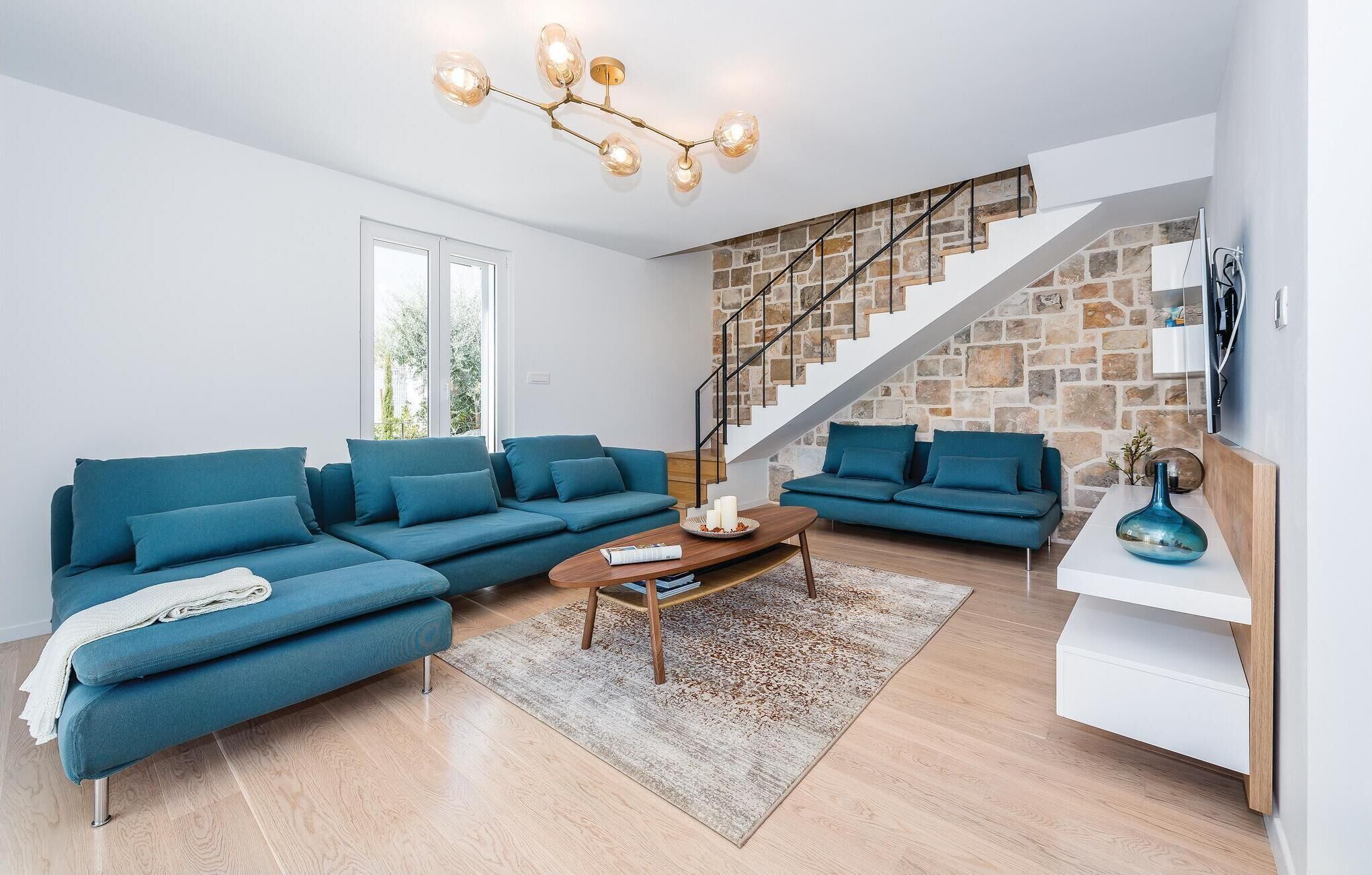 A modern living room with two blue sofas, a wooden coffee table, and a staircase with stone walls.