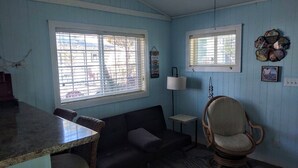 Una habitación con una mesa de comedor, un sofá, una mecedora y dos ventanas con persianas.