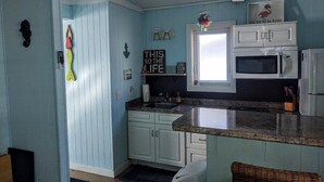 Una cocina con paredes azul claro, gabinetes blancos, una encimera de granito y un microondas.