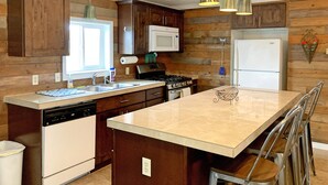 Une cuisine avec un lambris en bois, un îlot central, des appareils électroménagers en acier inoxydable et des luminaires suspendus.
