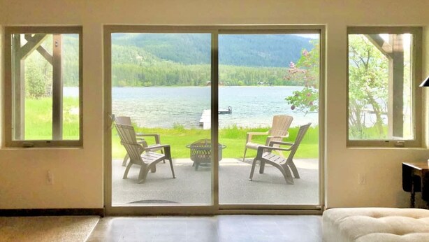 Una stanza con una porta scorrevole in vetro che dà su una terrazza con due sedie e un tavolino, affacciata su un lago e dolci colline boscose.