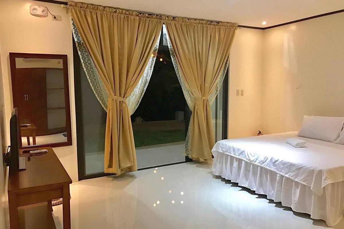 A hotel room with a bed, a desk, a mirror, and curtains.