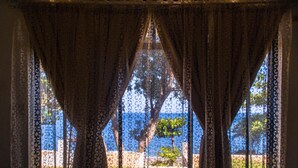 A view through a window with patterned curtains, revealing a tree and a body of water. - Bentrina Diving Resort (Mabini)