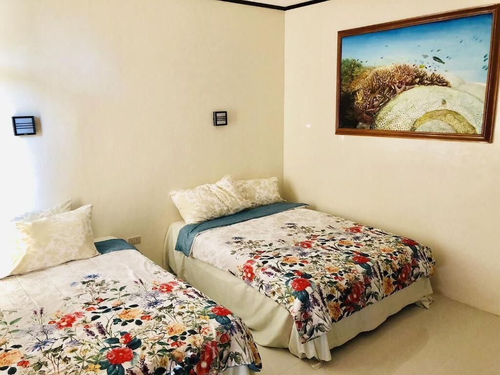 A bedroom with two beds, each with floral bedding, a painting on the wall, and a small nightstand.