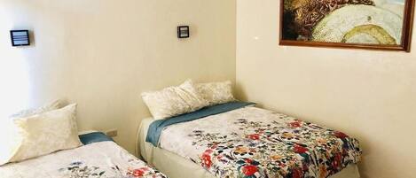 A bedroom with two beds, each with floral bedding, a painting on the wall, and a small nightstand.