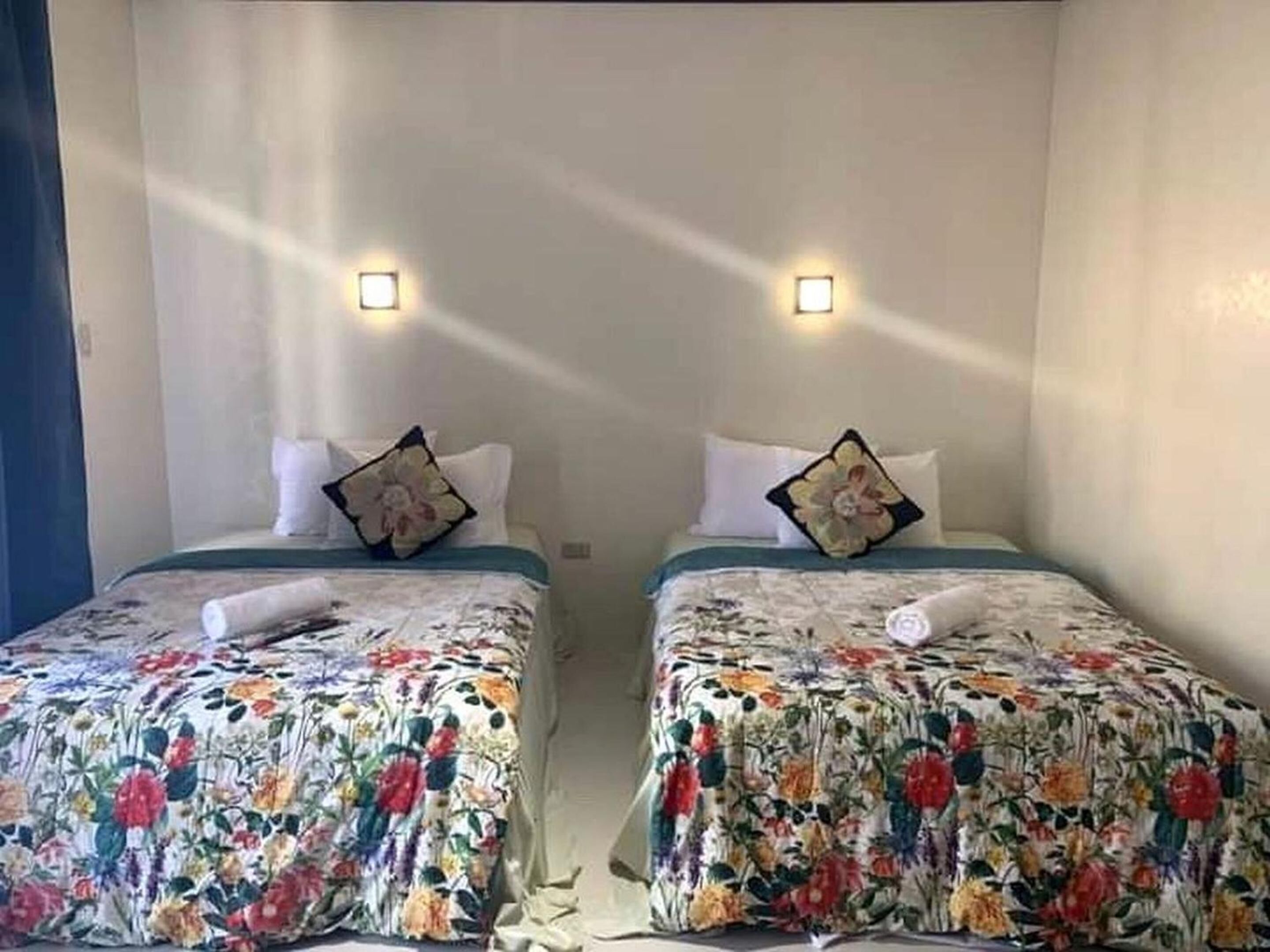 Habitación de hotel con dos camas individuales, cada una con ropa de cama estampada con motivos florales y almohadones decorativos.