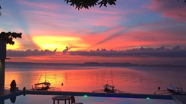 A sunset view from an infinity pool overlooking a calm sea with boats and a distant shoreline. - Bentrina Diving Resort (Mabini)