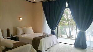 A hotel room with two beds, a nightstand, a lamp, and a view of the outdoors through large windows. - Bentrina Diving Resort (Mabini)