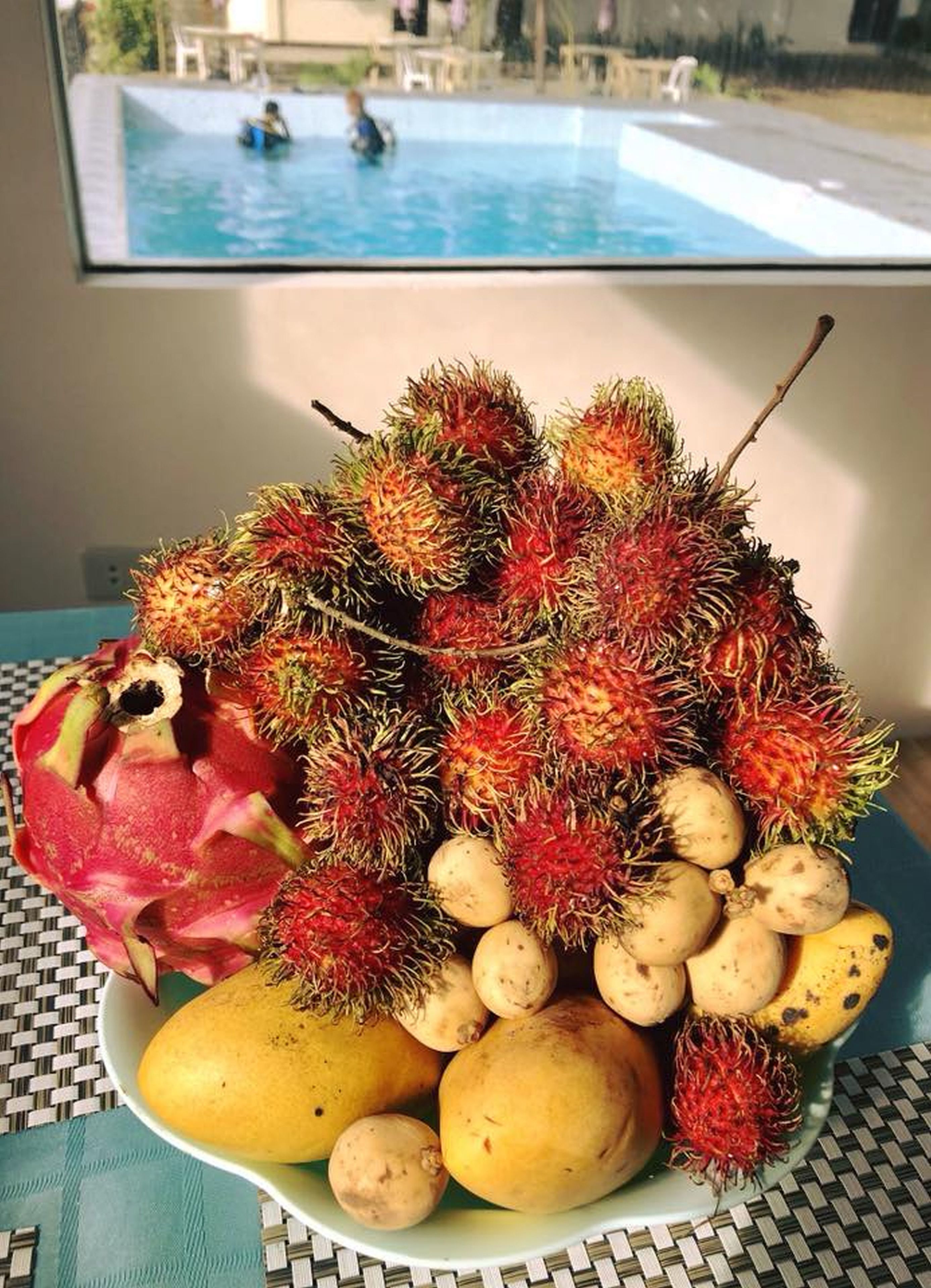 A table with a plate of rambutan, dragon fruit, and mangoes.