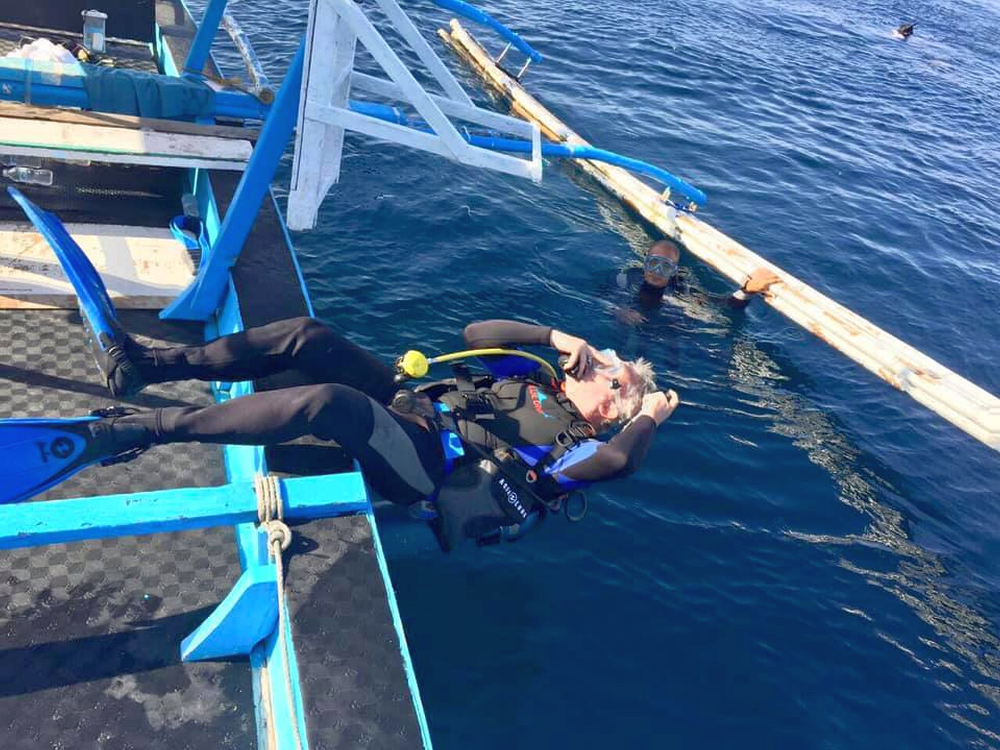A diver lying on a boat's deck, wearing a scuba diving suit and equipment.
