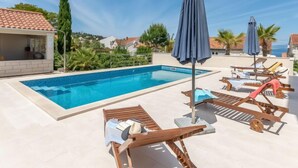 En swimmingpool med liggestole og parasoller, omgivet af en klar himmel og huse i baggrunden.