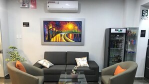 A modern hotel lobby with a black sofa, two armchairs, a glass coffee table, and a colorful painting above the sofa. - Palm Hotel (Tarapoto)