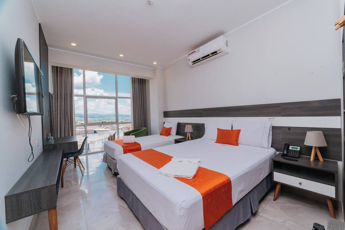 Une chambre d’hôtel avec deux lits, un bureau, une chaise, une télévision et une vue sur la ville.