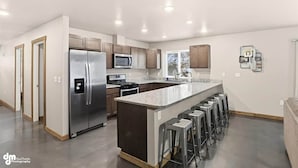 A modern kitchen with a central island, stainless steel appliances, and bar stools. - Matanuska Villa #1, Glacier Suites - Matanuska Villa #1 (Matanuska-Susitna)