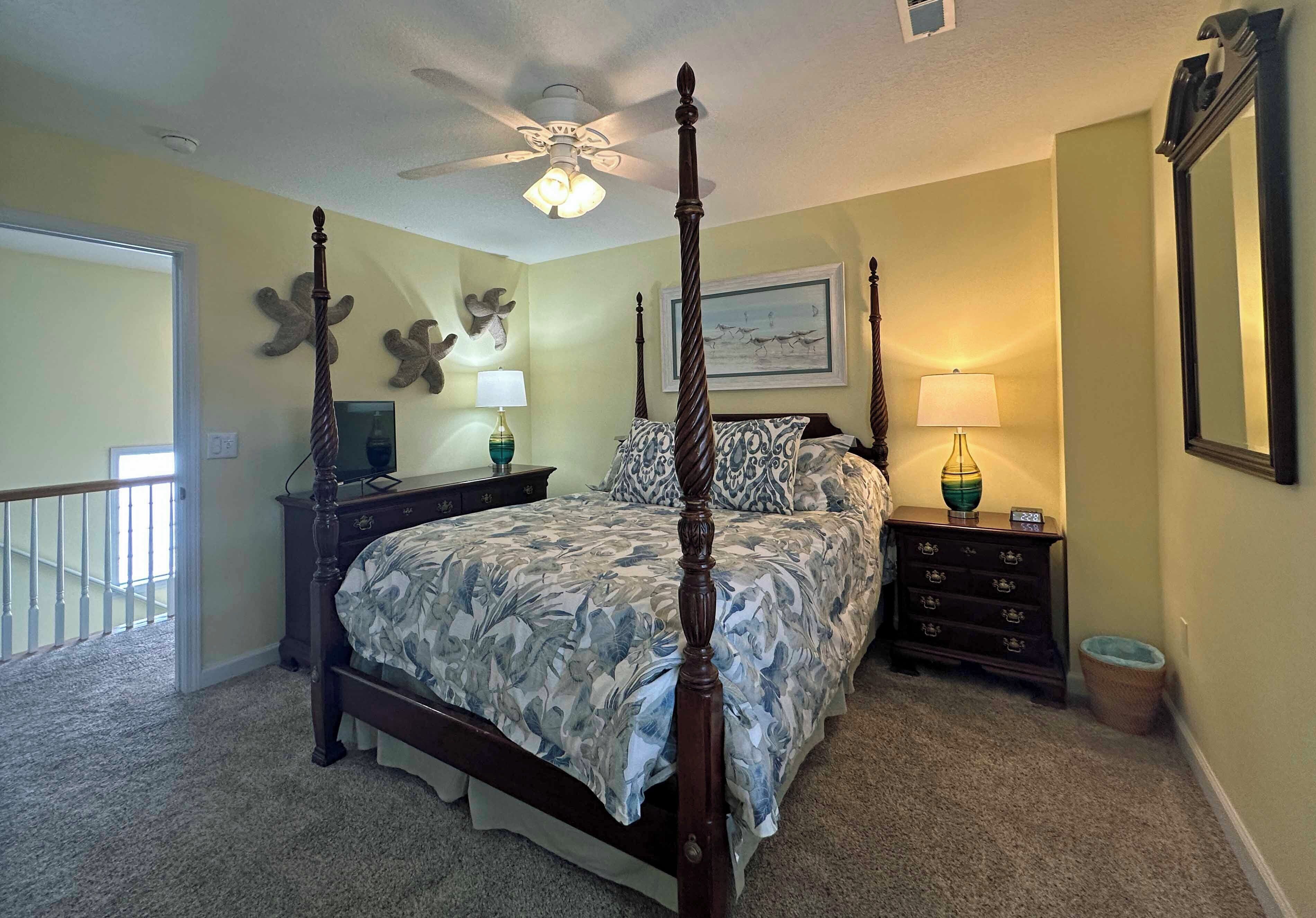 A bedroom with a four-poster bed, a nightstand, a dresser, a ceiling fan, and a large mirror.