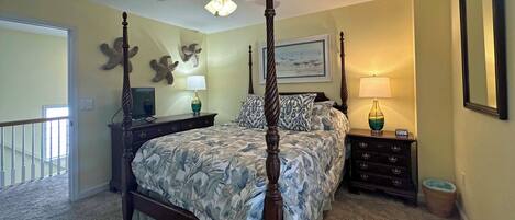 A bedroom with a four-poster bed, a nightstand, a dresser, a ceiling fan, and a large mirror.