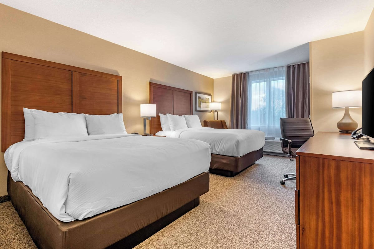 A hotel room with two beds, a desk, and a chair.
