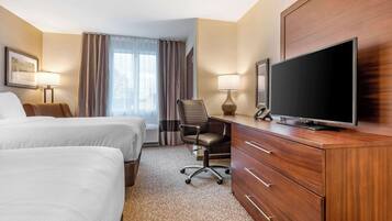 A hotel room with two beds, a desk with a flat-screen TV, a chair, and a wardrobe.