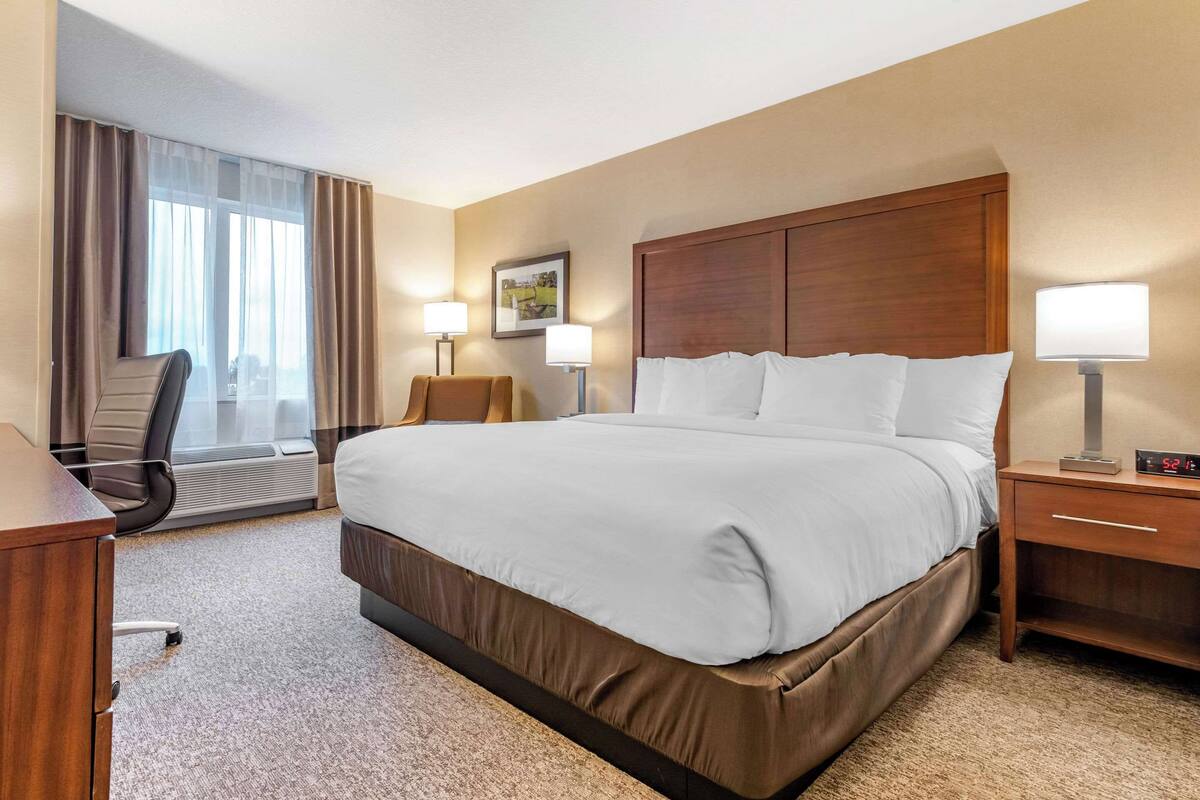 A hotel room with a large bed, a desk, a chair, and a window with curtains.