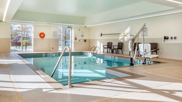 A modern indoor swimming pool with clear signage, a sunlit area, and a seating arrangement near the pool. - Comfort Inn & Suites (Goderich)