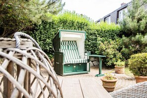 A wicker chair with a green and white striped cushion, a small table, and potted plants in an outdoor setting with a wooden deck and dense greenery. - Munkhoog - Munkmarsch (Munkmarsch)