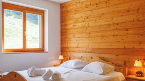 Ein hölzernes Bett mit weißen Leinentüchern, ein Nachttisch mit Lampe und ein Fenster mit Blick auf eine grüne Landschaft.