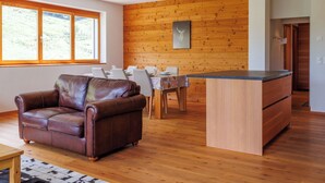 Ein modernes Wohnzimmer mit Ledersofa, Holzboden, einem Essbereich mit Tisch und Stühlen sowie einer Kücheninsel.