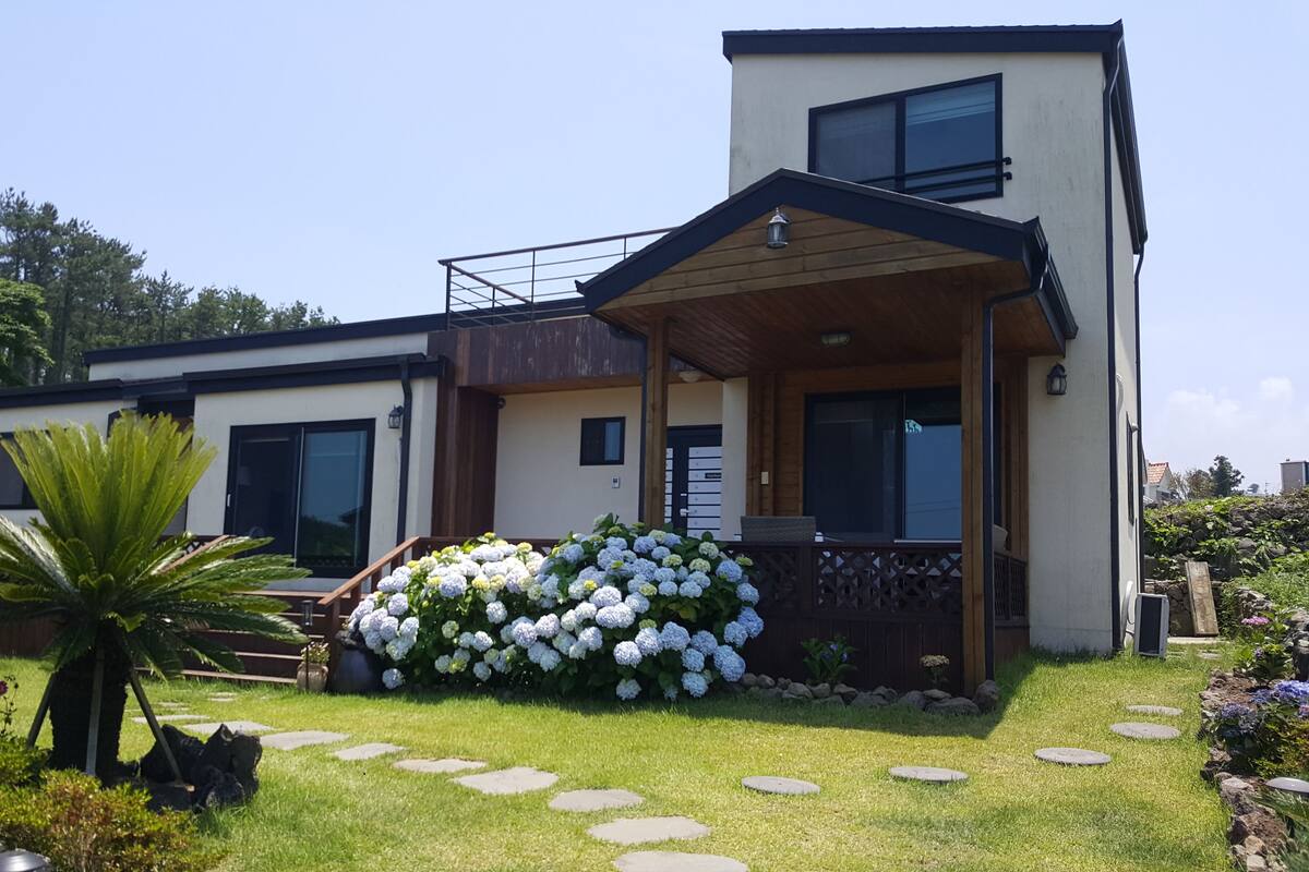 A modern two-story house with a covered porch, a well-maintained lawn, and a large flower bed.
