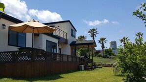 A modern two-story house with a covered patio area, a wooden fence, and a grassy yard. - Sonangche (Jeju City)