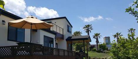 A modern two-story house with a covered patio area, a wooden fence, and a grassy yard.