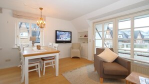 Een gezellige woonkamer met een eethoek, een aan de muur bevestigde televisie en grote ramen met uitzicht op de omgeving.