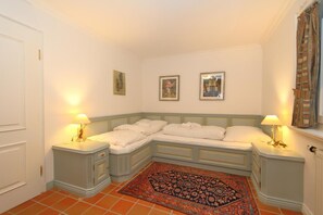 A corner bedroom with a bed, two bedside tables, a patterned rug, and framed pictures on the wall. - Mecking Munkmarsch<br>The Mecking apartment is a lovingly furnished, fully equipped, modern and quietly located vacation home. (Munkmarsch)