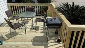 A wooden deck with a glass table and metal chairs, a barbecue grill, and a wooden fence. - Cottage:  3005 Palmetto Blvd. (Edisto Beach)
