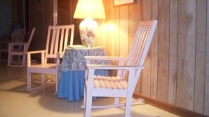 A wooden-paneled room with two white rocking chairs, a small table with a blue tablecloth, and a lamp. - Cottage:  3005 Palmetto Blvd. (Edisto Beach)
