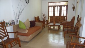 A living room with a sofa, wooden chairs, a table, and a window with decorative glass. - 1 and 1 (Malimbada)