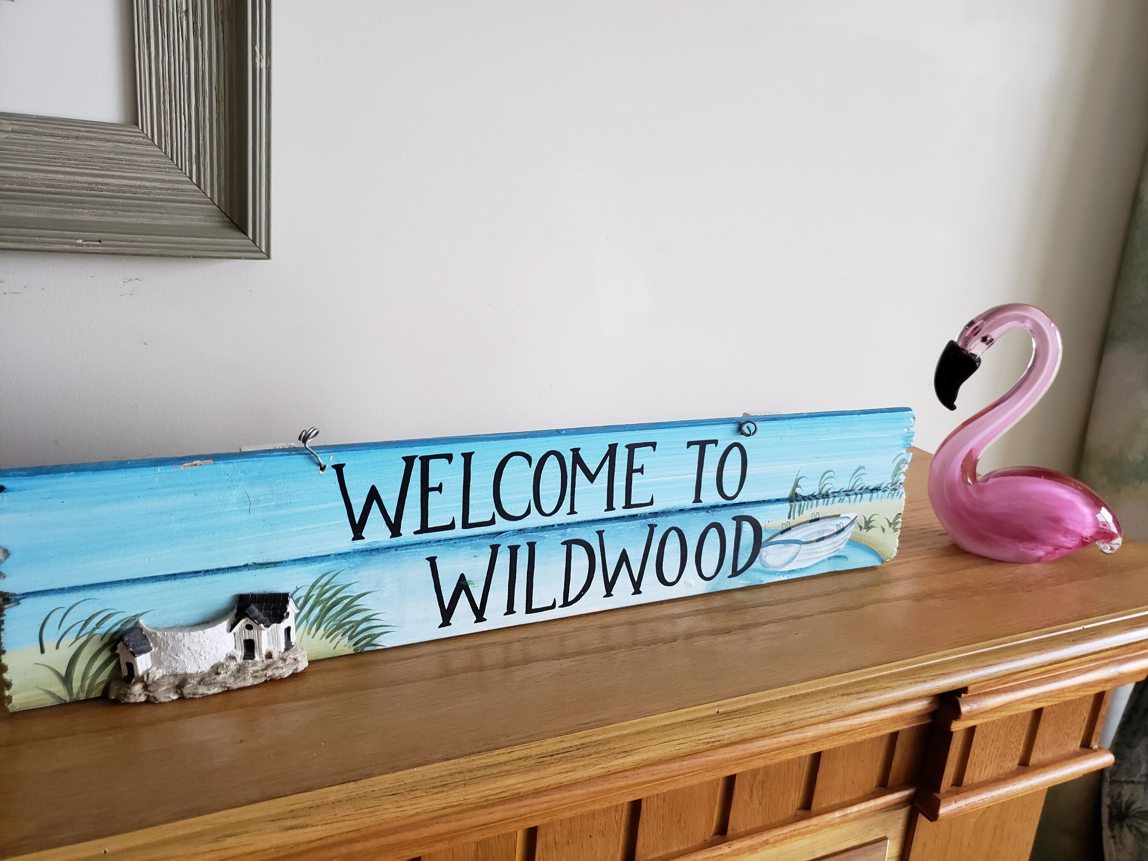 Un letrero de madera con la inscripción "WELCOME TO WILDWOOD" y un flamenco rosa.