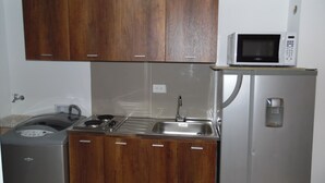 Eine kleine Küche mit Holzschränken, einer eingebauten Mikrowelle, einer Edelstahl-Spüle und einem kompakten Kühlschrank.