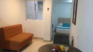 Ein gemütliches Zimmer mit einer Couch, einem kleinen Tisch mit Früchten, einem Bett mit blauer und weißer Bettdecke und einem Fenster mit Blick.