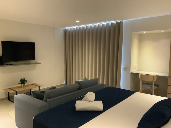 A modern hotel room with a bed, a sofa, a TV, and a desk.