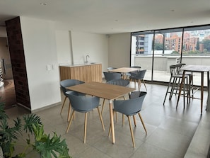 A modern kitchen with a wooden countertop and a sink, a dining area with a wooden table and blue chairs, and a large window with a city view.