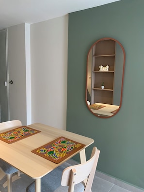 A dining area with a table, chairs, a mirror, and a shelf with decorative items.