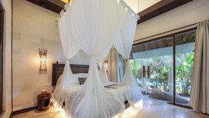 Un dormitorio con una cama de dos columnas con dosel, cabecera de madera y vistas a exuberante follaje a través de una puerta corrediza de vidrio.