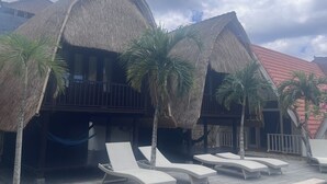 Ein Resort mit strohgedeckten Häusern, Liegestühlen und Palmen.