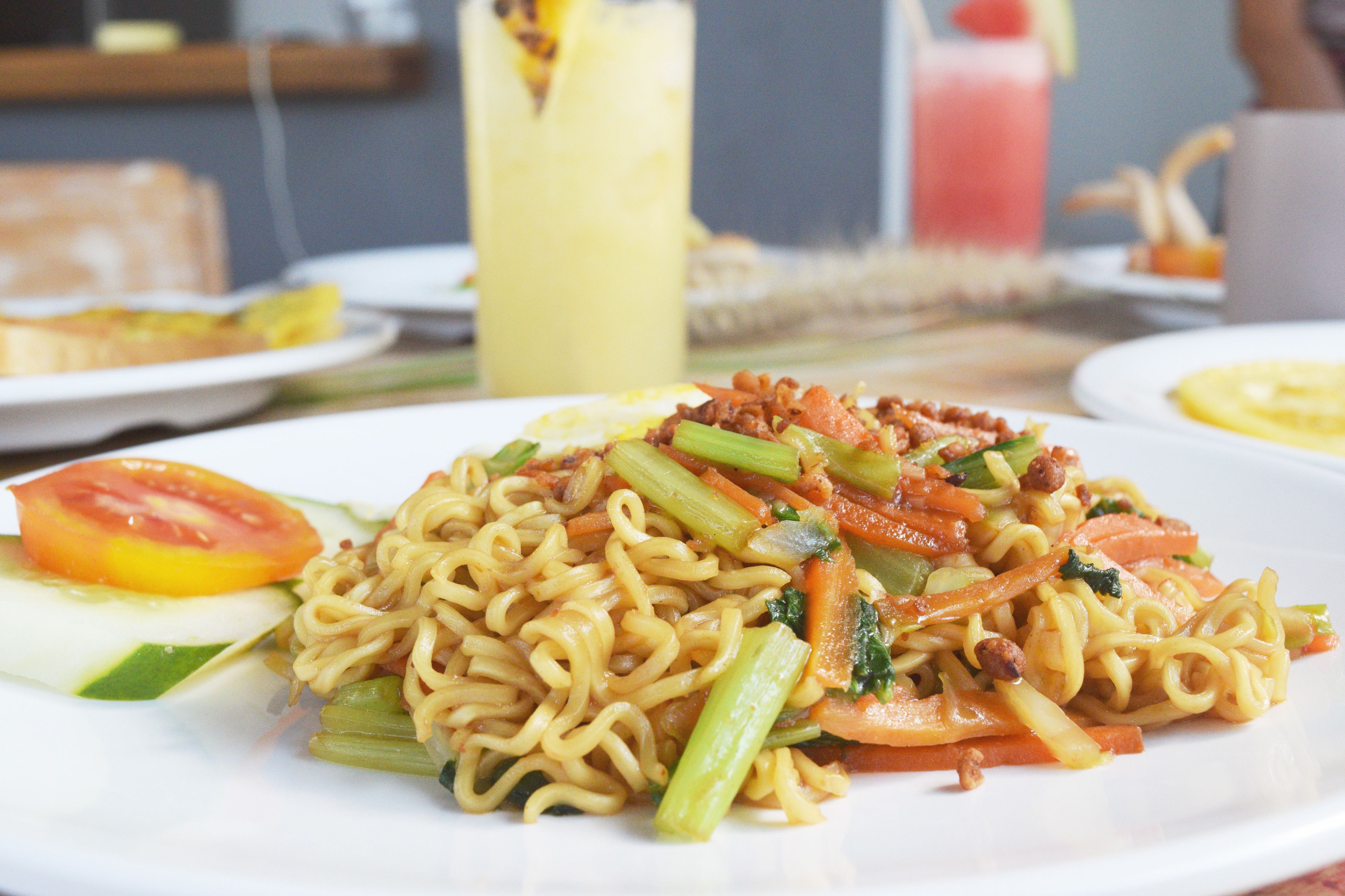 Un piatto di noodles con verdure e una fetta di pomodoro.